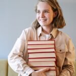 woman in beige blazer holding red book