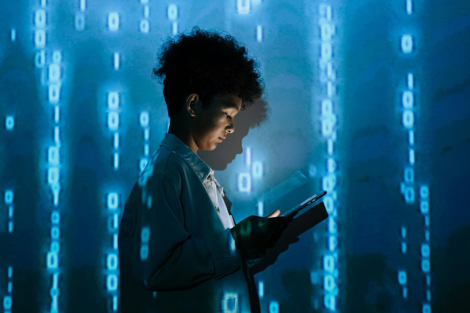 young person holding a tablet and standing on the background of a projection of numbers
