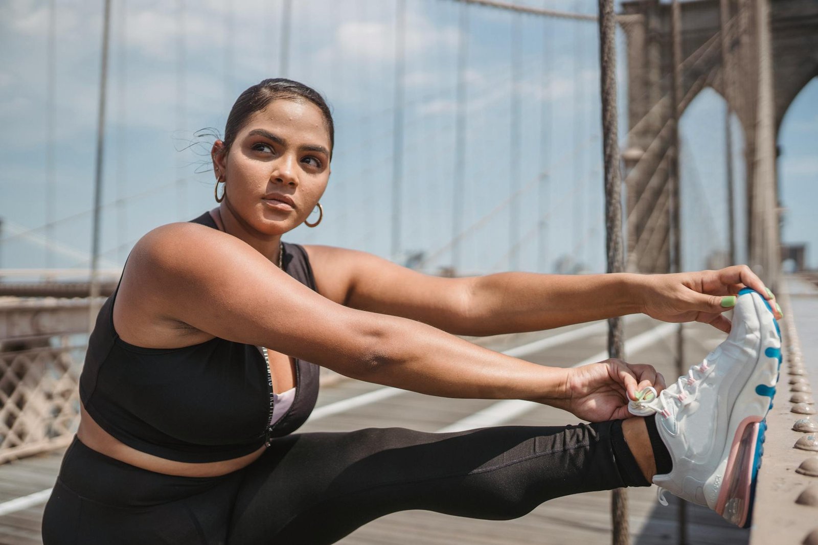 woman in sneakers stretching on bridge