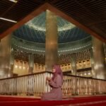 woman praying inside a grand mosque interior