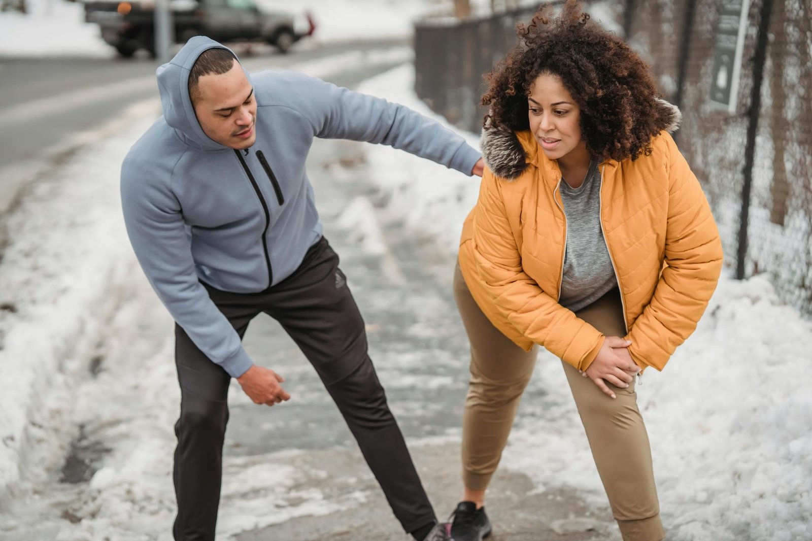 black trainer helping plump african american woman to stretch on snowy walkway