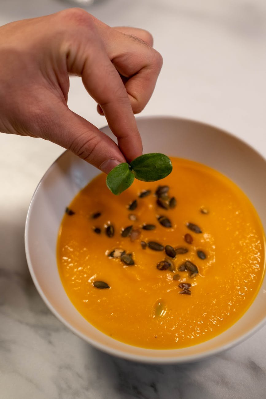 a person putting garnish on a pumpkin soup