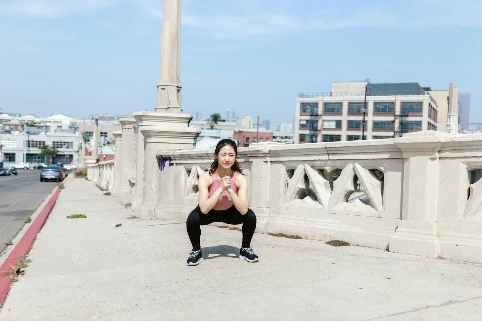 woman wearing pink top and leggings doing low squats on sidewalk