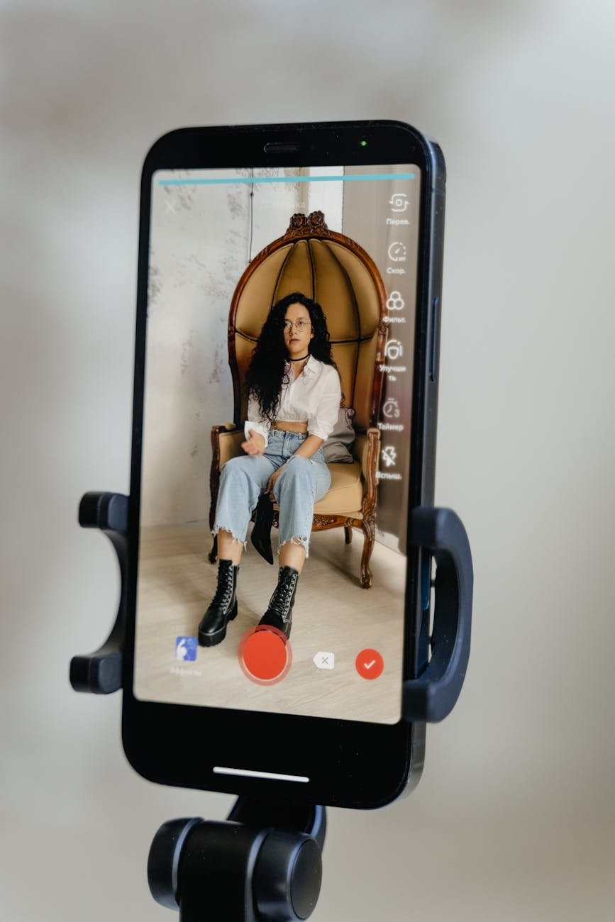 smartphone screen displaying a woman in white long sleeve shirt sitting on armchair