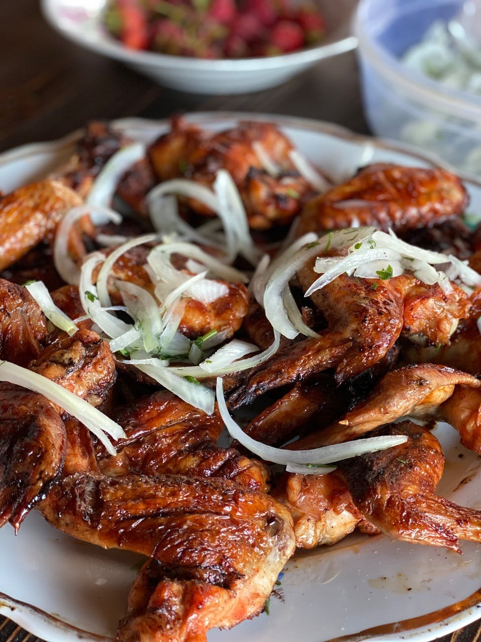 cooked chicken wings with white sliced white onion on top on white ceramic plate