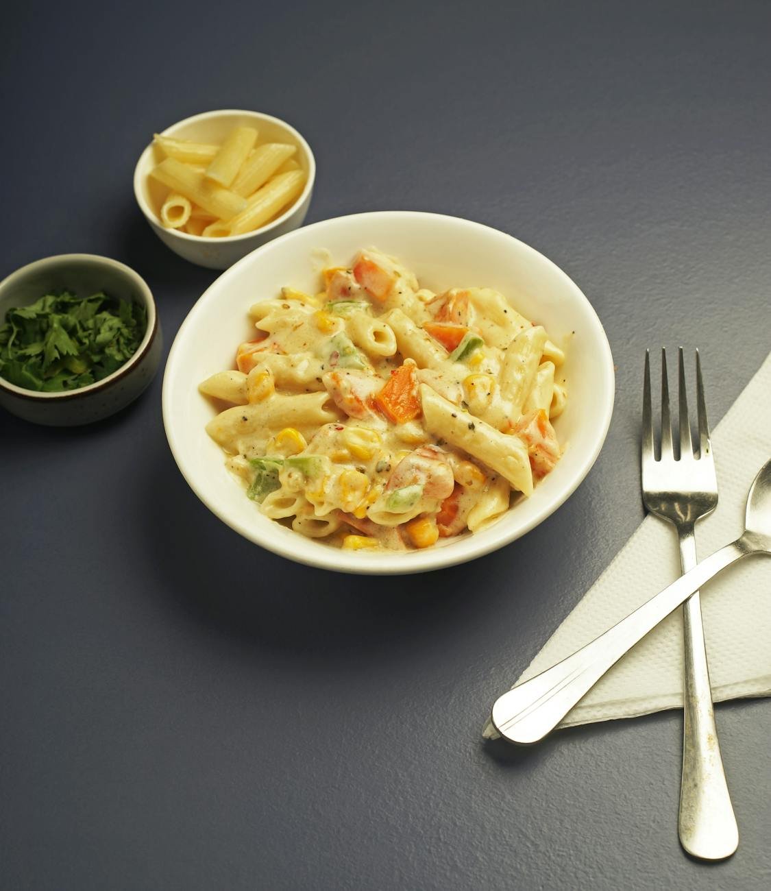 creamy penne pasta with vegetables on blue table