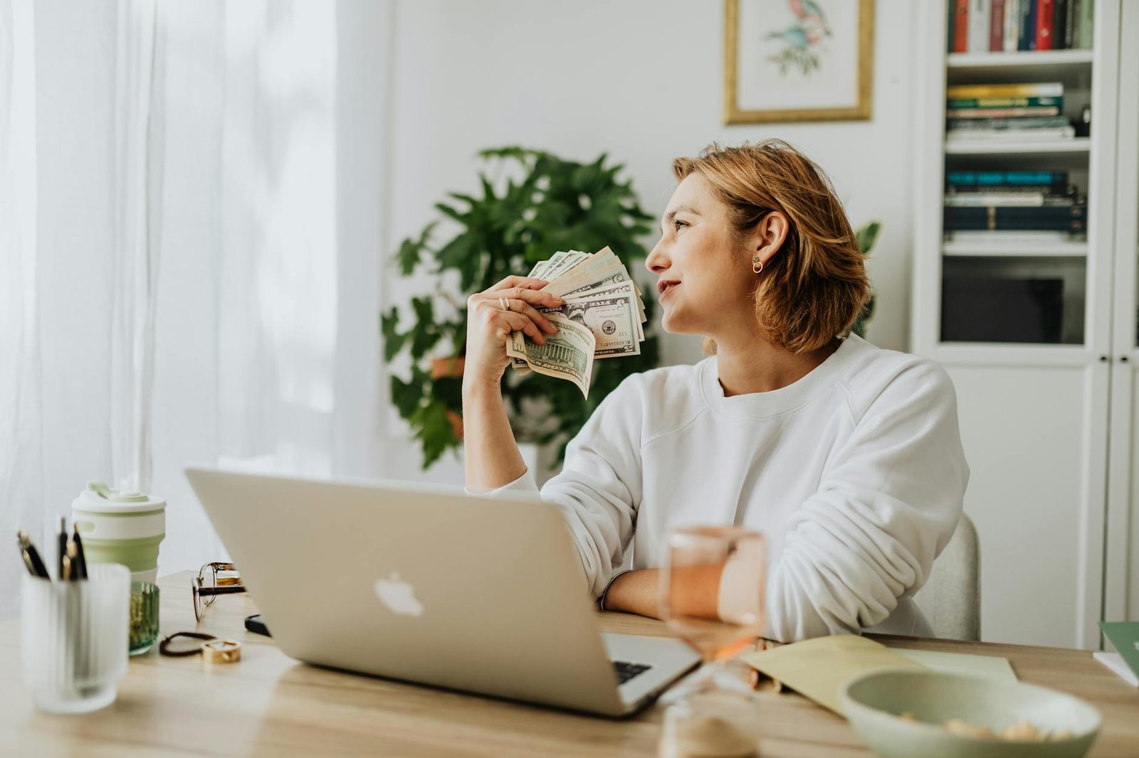 woman sitting and holding money with laptop on desk