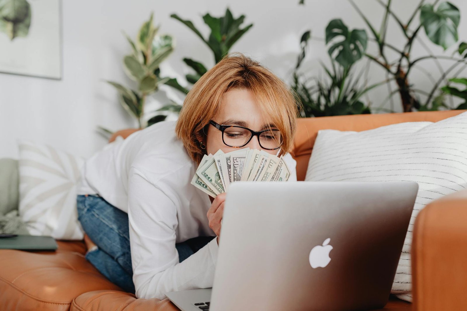 woman sitting on a couch in front of a laptop and covering her face with money