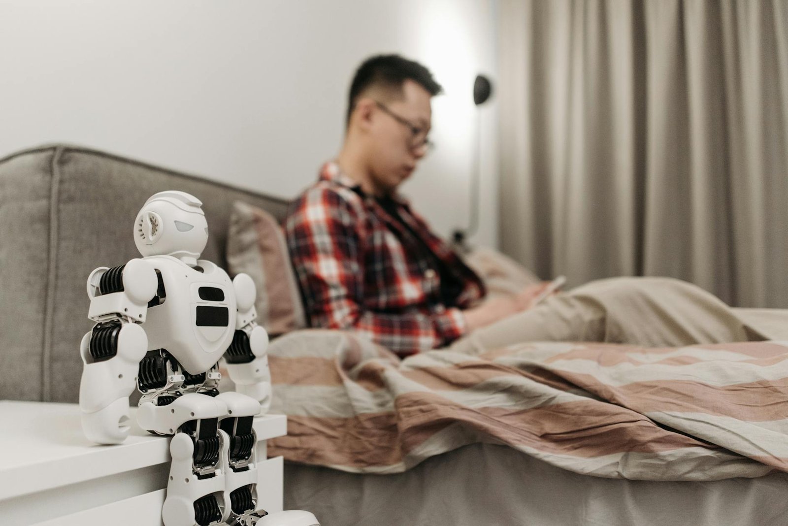 a man sitting on the bed near the white robot on the bedside table